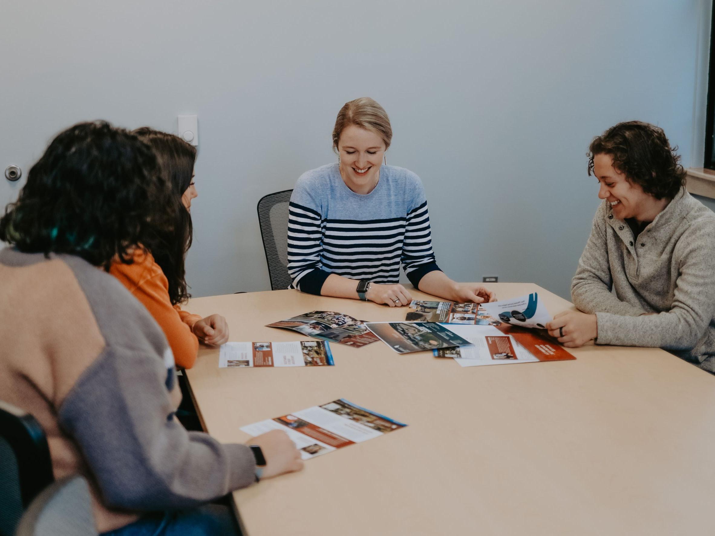 Director of Admissions sits around a table with three students looking at print materials